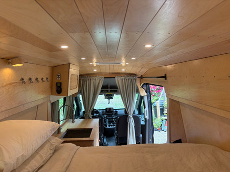 Inside this modern van conversion for rv rental: a cozy bed, sleek kitchen, and warm wood-paneled interior. Ready for adventure!