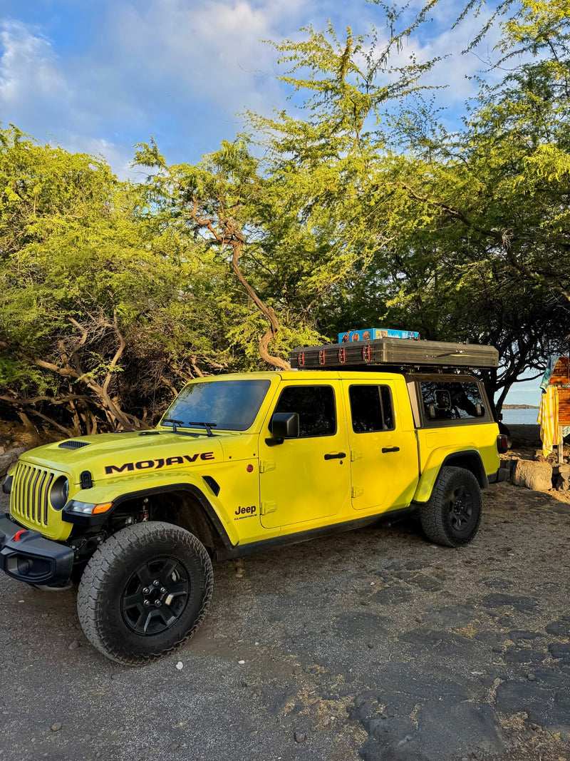 Bright yellow Jeep Gladiator Mojave with a rooftop tent, perfect for an RV rental adventure, parked among trees near the water. — photo 9