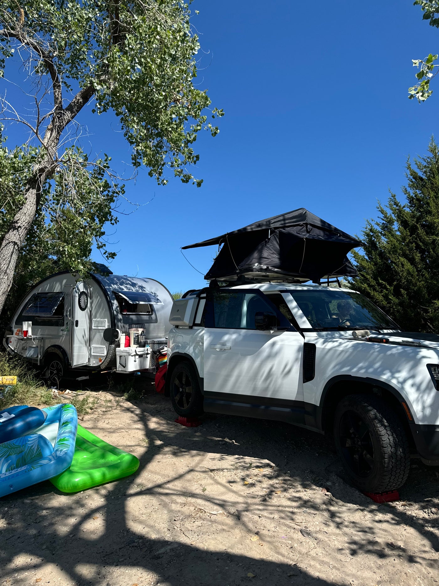 A white SUV with a rooftop tent and a nuCamp teardrop trailer parked at a sunny campsite, perfect for an rv rental getaway. — photo 19