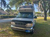 Airstream camper van RV rental parked on grass by road under Spanish moss trees. Front view of gray van.