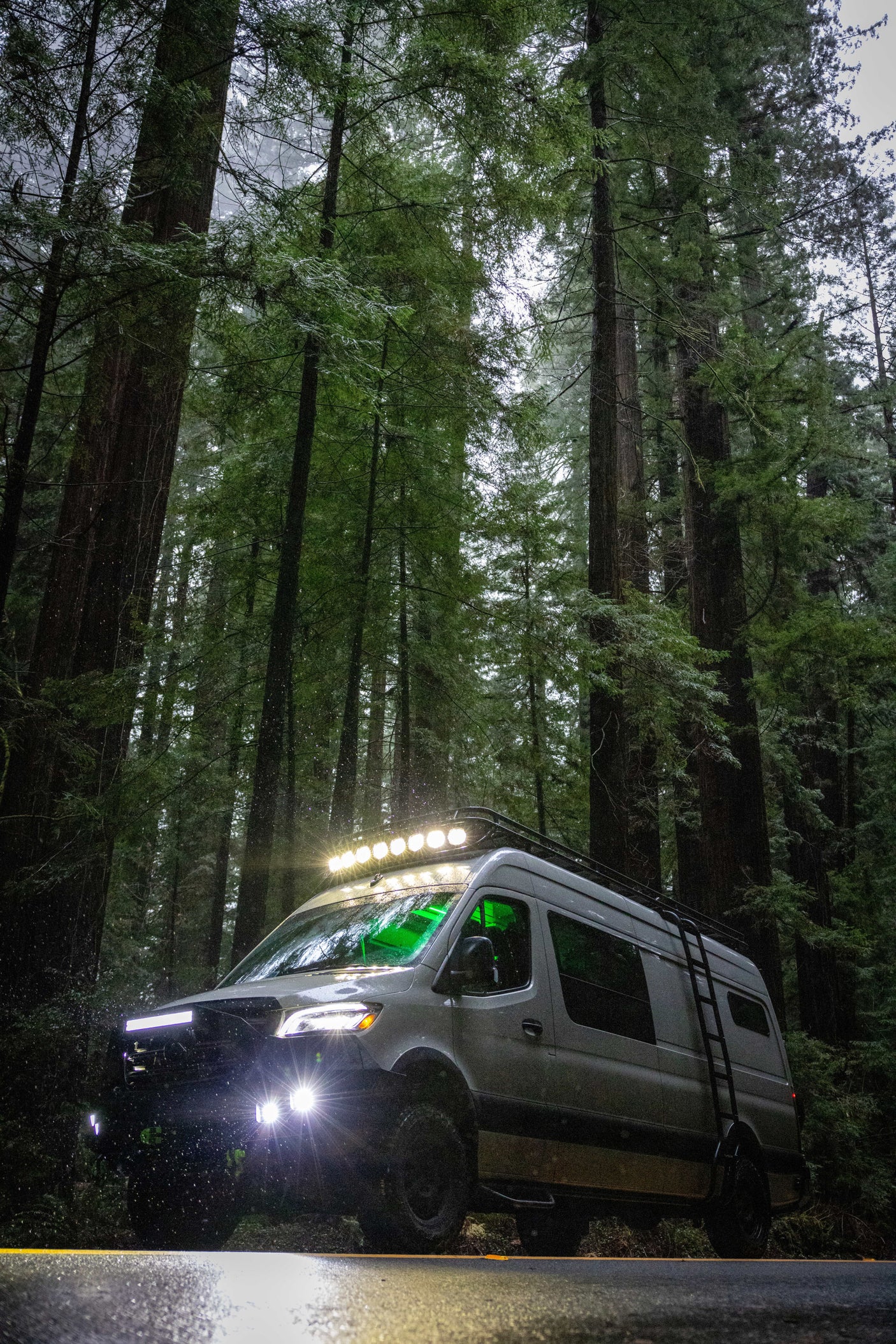 Off-road RV rental van lighting up a misty redwood forest road, ready for adventure among towering trees.