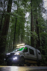 Off-road RV rental van lighting up a misty redwood forest road, ready for adventure among towering trees.