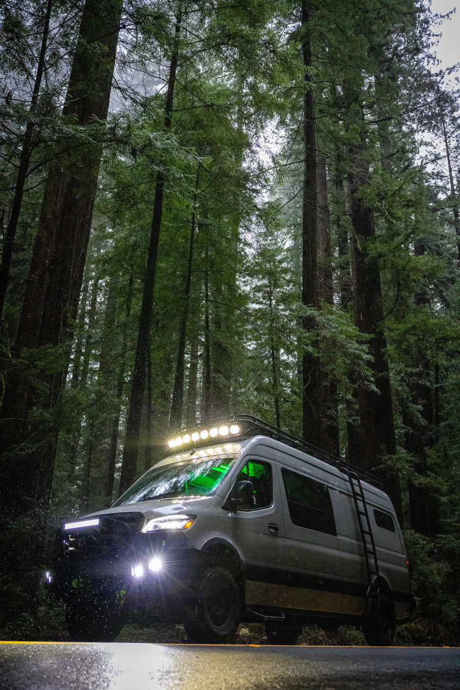 Off-road RV rental van lighting up a misty redwood forest road, ready for adventure among towering trees.