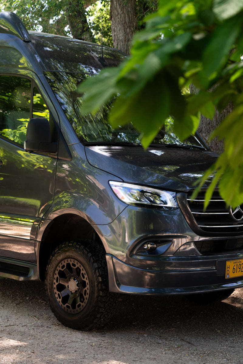 Dark gray Mercedes Sprinter camper van, an RV rental, with off-road tires, parked outdoors beneath leafy trees. — photo 18