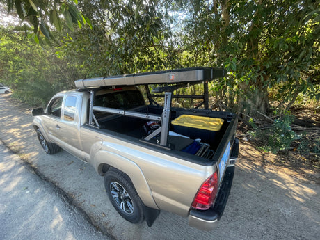 Tan Toyota Tacoma pickup with a bed rack & rooftop tent, full of camping gear. A perfect RV rental for rugged adventures.