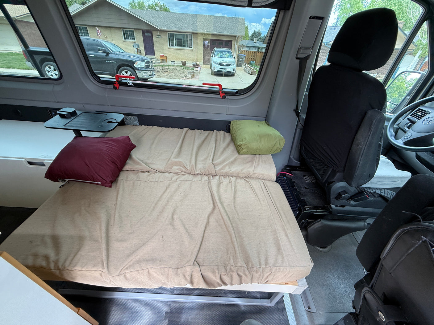 Inside this RV rental camper van: a comfy bed, table, and storage. View of a residential street. Perfect for your road trip!