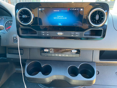 Modern rv rental dashboard featuring an infotainment screen with Apple CarPlay prompt, climate controls, and cup holders.