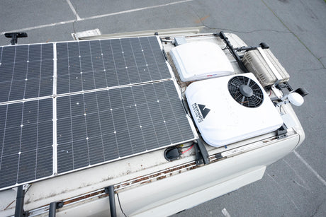 Overhead view of an RV rental's roof with large solar panels, Nomadic Cooling AC, and MaxxAir fan for comfortable off-grid trips.