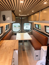 Explore this modern rv rental interior: wood slat ceiling, plush brown seating, dining tables, and bright lighting.
