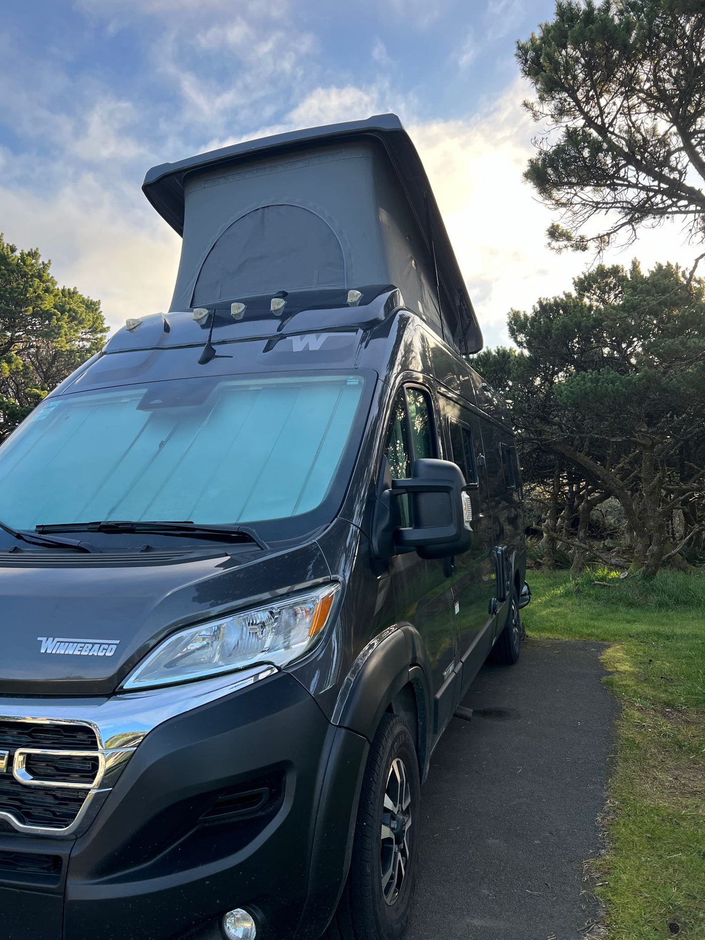  perfect for an rv rental adventure.|Experience coastal beauty! Dark RV rental camper van parked at a scenic overlook with a vast beach & ocean.|Enjoy an RV rental camping experience! A Winnebago Solis at a tree-lined campsite with a burning fire pit.|Experience comfort in this rv rental. Features include a compact kitchen — photo 2