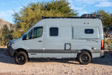 Side view of a gray Winnebago Revel 4x4 camper van parked on a dirt road. Ideal for an RV rental adventure.