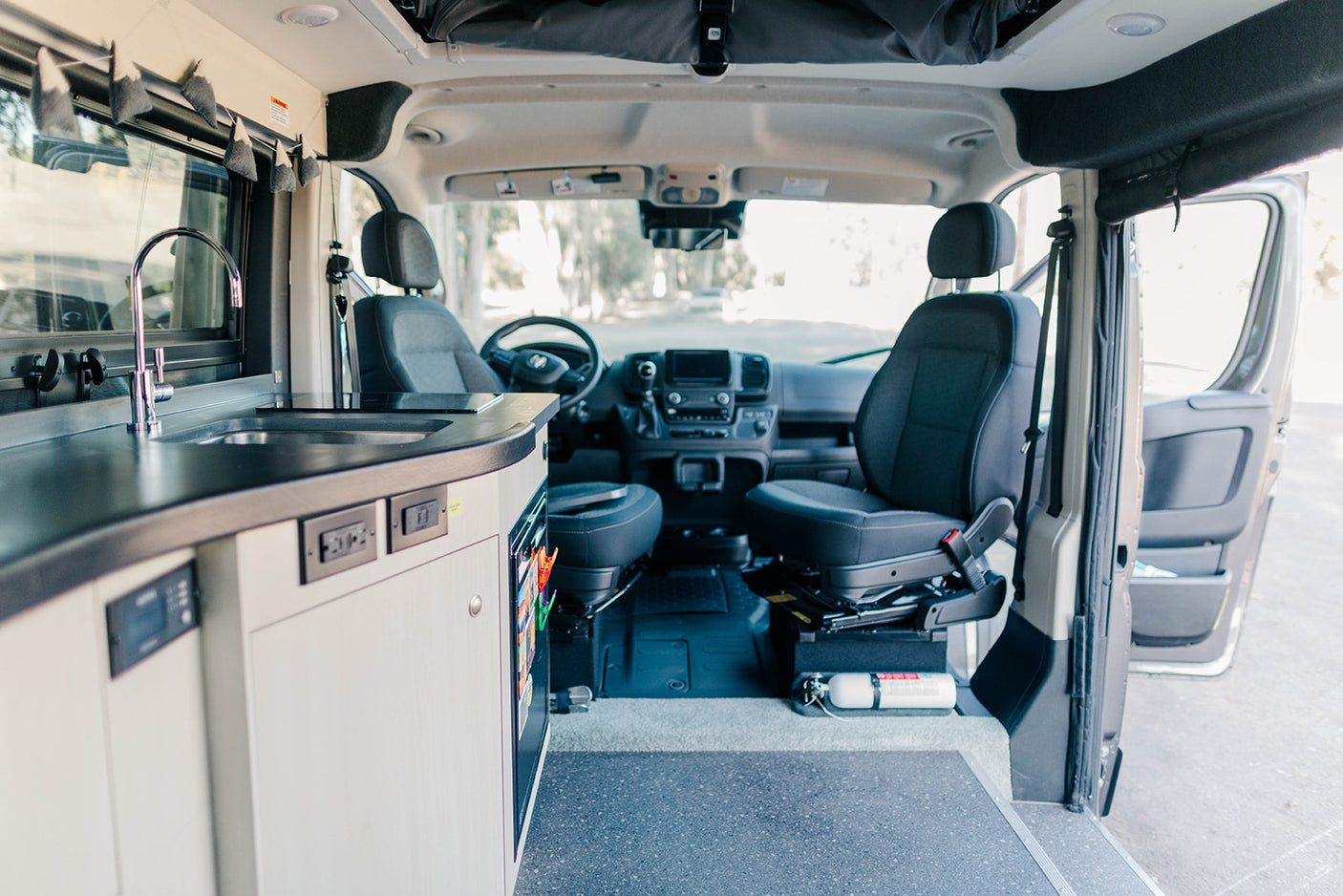 Inside a well-equipped RV rental, showcasing a kitchen, comfortable front seats, and safety essentials like a fire extinguisher.
