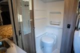 Compact rv rental interior featuring a functional bathroom with toilet, shower, and mirror, adjacent to the bed and sink area.