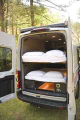 Inside this RV rental, dual bunk beds and pull-out storage are visible at the rear of a parked camper van.