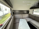 Spacious RV rental interior with a gray sectional couch and marble-look table; bright windows show an outside trailer.