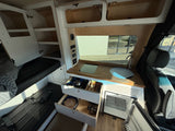 RV rental interior: cozy camper van with kitchenette, open drawers, fridge, and built-in storage.