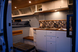 Step inside this stylish RV rental van! Features a compact kitchen, comfortable bed, and warm lighting.