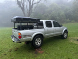 An RV rental alternative: a silver Toyota Tacoma pickup with a rooftop tent and gear, parked on grass in a foggy landscape.