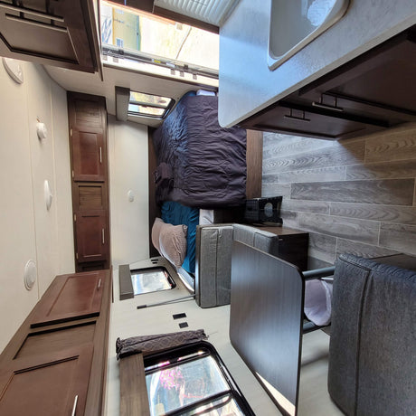 Inside an RV rental: view of the cozy bed, dining area, and modern wood-look interior.