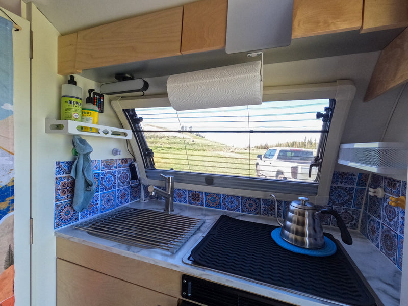 This RV rental's compact kitchen features a sink, kettle, tiled backsplash, and a window with outdoor views. — photo 14