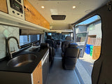 RV rental interior: kitchen with sink, cooktop, wood cabinets, and comfortable seating visible from the rear.