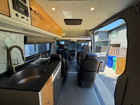 RV rental interior: kitchen with sink, cooktop, wood cabinets, and comfortable seating visible from the rear.