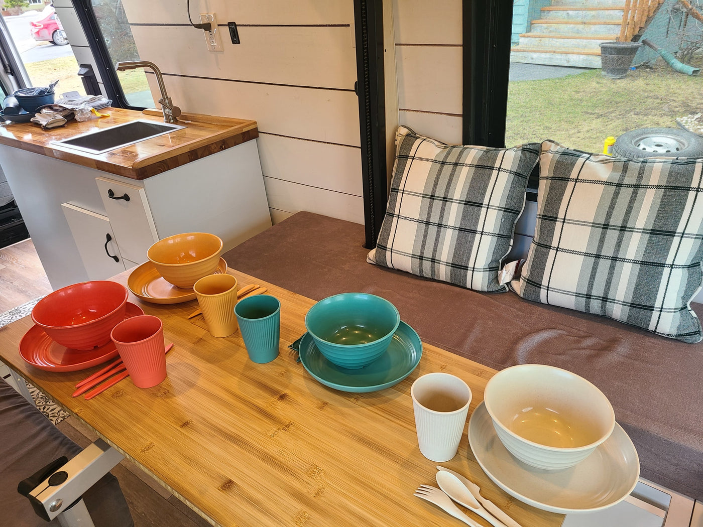 Inside a modern RV rental: a compact kitchen, cozy dining table with colorful dishes, and plaid bench cushions. — photo 3