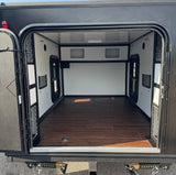 Inside an RV rental: a clean, empty camper interior with dark wood floor, white walls, and built-in storage.