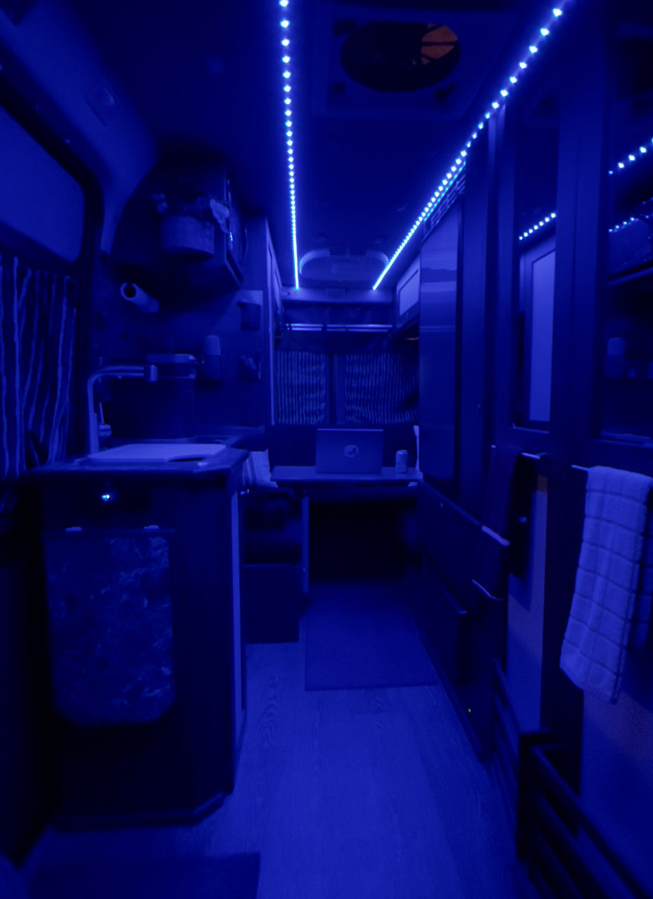 Experience mobile living in this blue-lit RV rental interior, featuring a compact kitchenette and a laptop workspace.