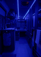 Experience mobile living in this blue-lit RV rental interior, featuring a compact kitchenette and a laptop workspace.