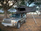 A grey Jeep Patriot SUV with a deployed Nomadic rooftop tent, an RV rental alternative for outdoor adventures.