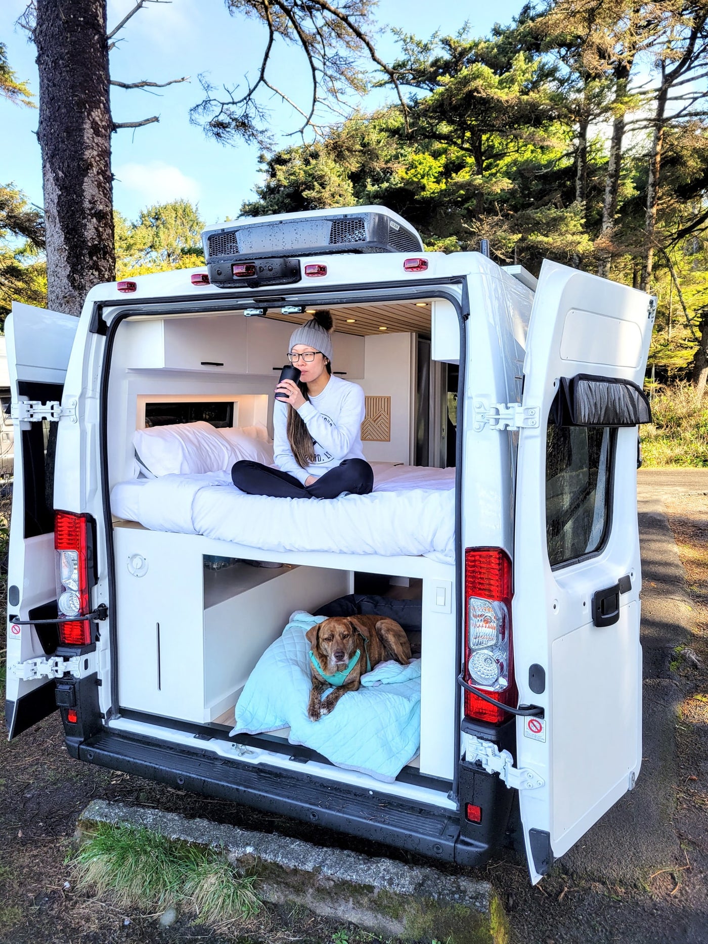 Cozy RV rental adventure: Woman sips coffee on bunk bed while dog rests below in a scenic camper van. — photo 20