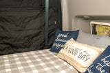Cozy RV rental bed with cheerful pillows, a plaid blanket, and a window view, offering a comfortable night's rest on the road.