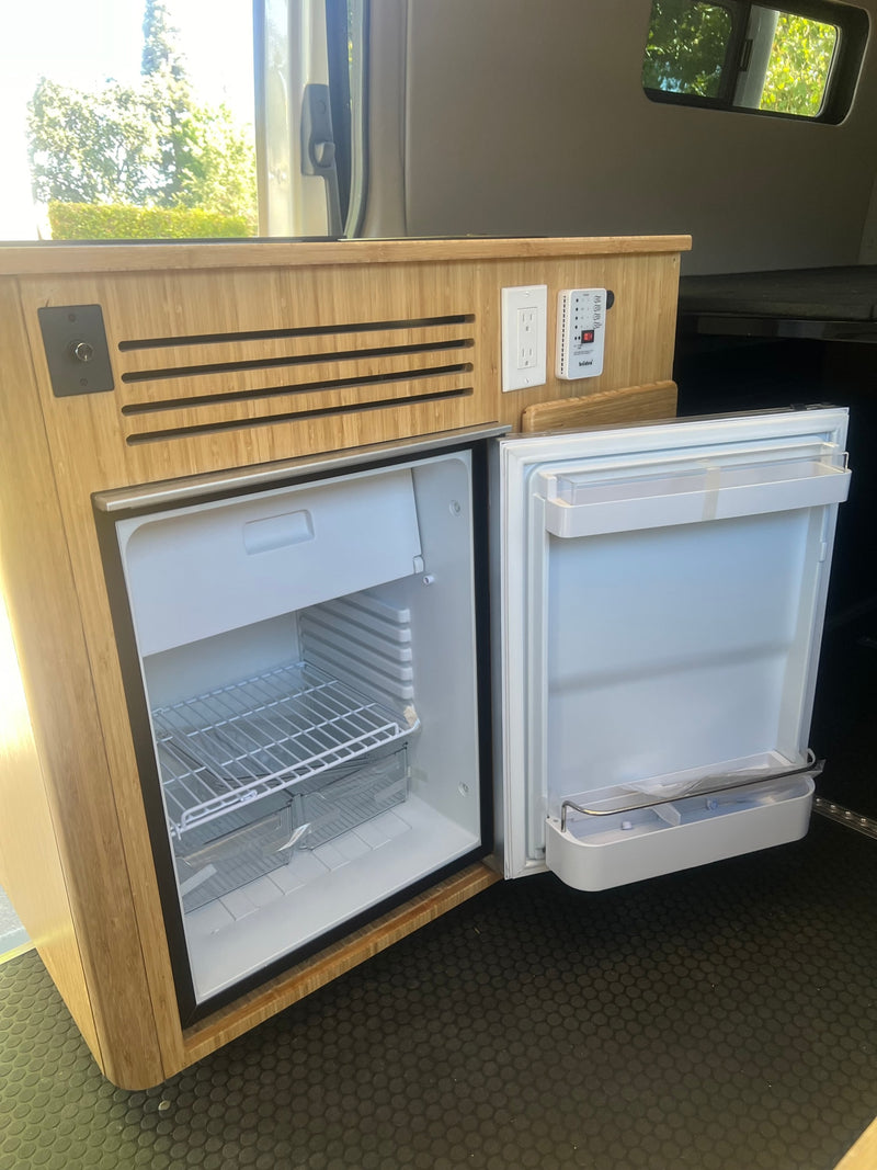 An RV rental interior with a built-in, open refrigerator/freezer in bamboo cabinetry, plus power outlets & a monitor. — photo 7