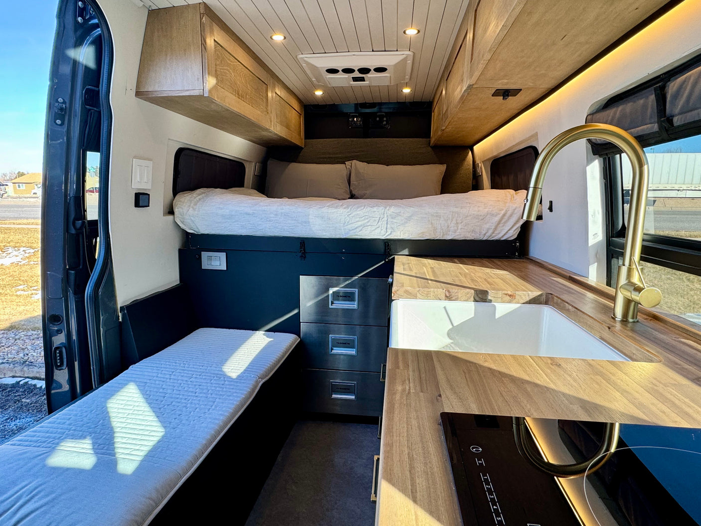 Spacious rv rental interior featuring a cozy bed, sleek kitchen with wood counters, sink, and cooktop, plus storage.