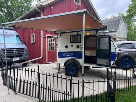Parked RV rental setup: a white teardrop camper with open door & awning, beside a gray Mercedes Sprinter van.