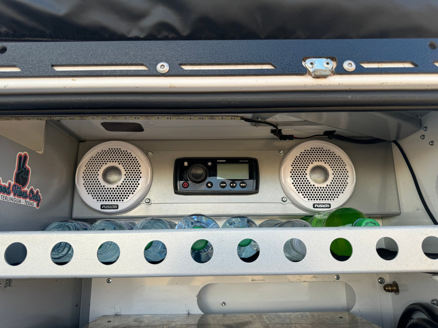 Custom RV rental setup features a Fusion stereo, speakers, and water bottles in a lit storage area. Good vibes! — photo 7