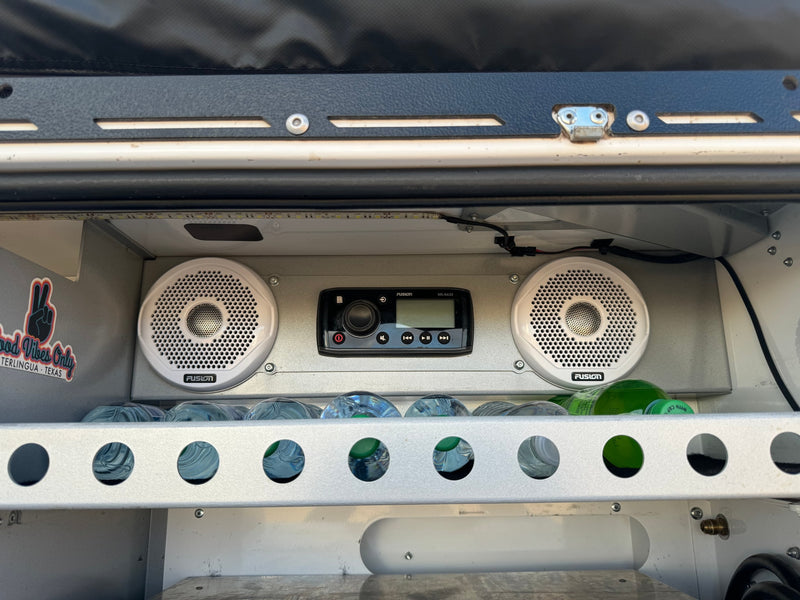 Custom RV rental setup features a Fusion stereo, speakers, and water bottles in a lit storage area. Good vibes! — photo 7