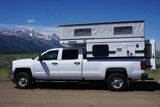 White Chevrolet 2500 HD RV rental truck camper with pop-up roof against mountains. Perfect for adventure camping.