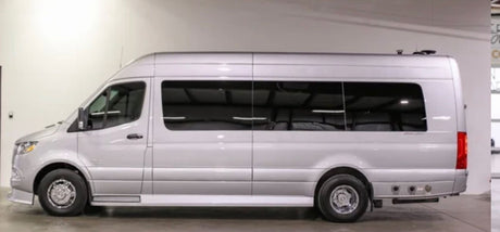 A silver Mercedes Sprinter RV rental. Side profile of a spacious, high-roof camper van in a showroom.