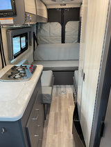 Step inside this cozy RV rental camper van, featuring a modern kitchen area, gray sofa bed, and practical storage solutions.