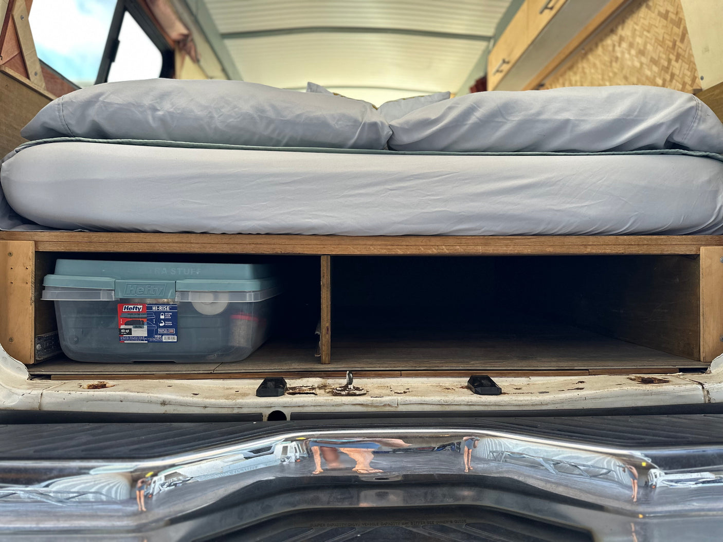 RV rental interior: Comfortable bed elevated over wooden storage compartments, holding a Hefty HI-RISE bin. Perfect for organizing travel gear.