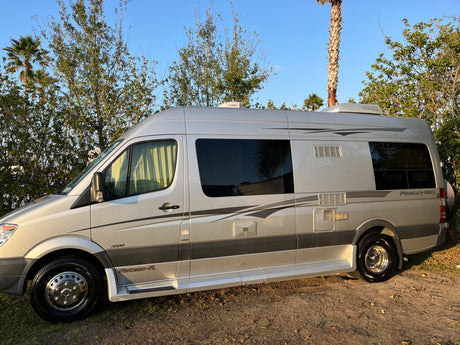 A sleek silver Pleasure-Way Plateau-FL Class B rv rental, parked outdoors on dirt, ready for your next adventure.