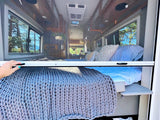 RV rental interior: A hand latches a screen door, revealing a cozy bed and stunning outdoor views from this camper van.