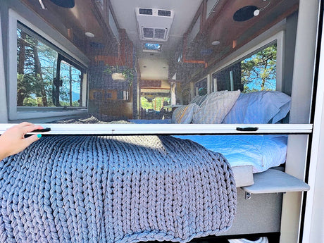 RV rental interior: A hand latches a screen door, revealing a cozy bed and stunning outdoor views from this camper van.