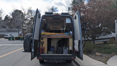 Rear view of a customized camper van with open doors, revealing a cozy bed and ample storage. Book your RV rental adventure!