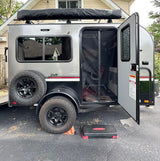 Compact off-road travel trailer, ideal for an RV rental adventure, parked in a driveway. The door is open, showing its interior.
