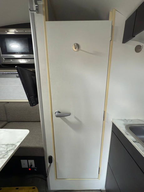 RV rental interior: kitchen with sink, microwave, dining booth with TV, and a central white door with a handle and hook.