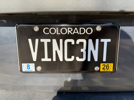 Colorado RV rental license plate "VINC3NT" with an August 2026 expiration sticker, seen on a vehicle's rear.