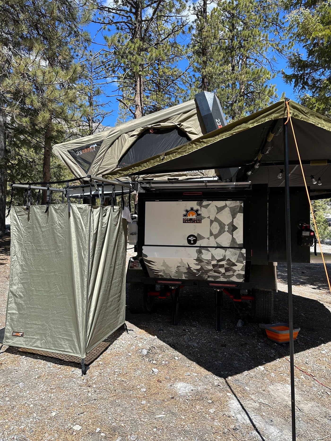 An olive green off-road camping trailer is set up with a rooftop tent, side awning, and privacy tent, perfect for an RV rental. — photo 16